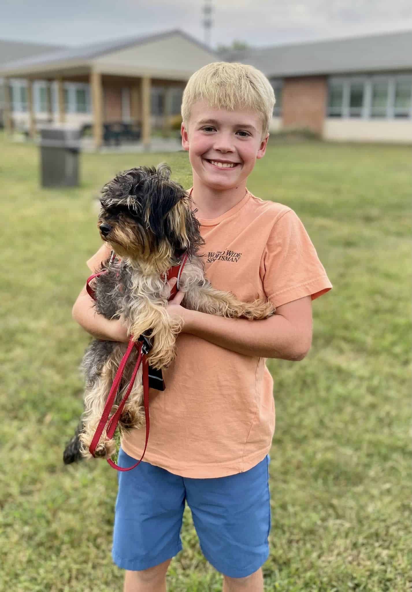 A young boy holding a small dog in front of a building.