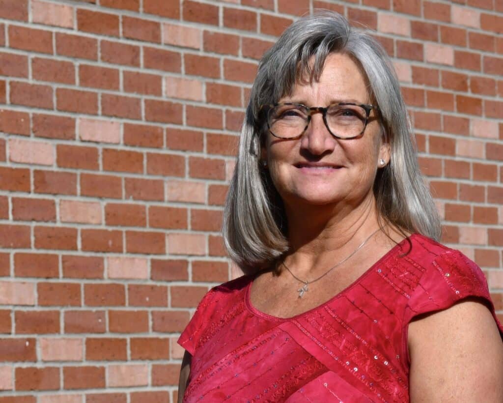 A woman in glasses standing in front of a brick wall.