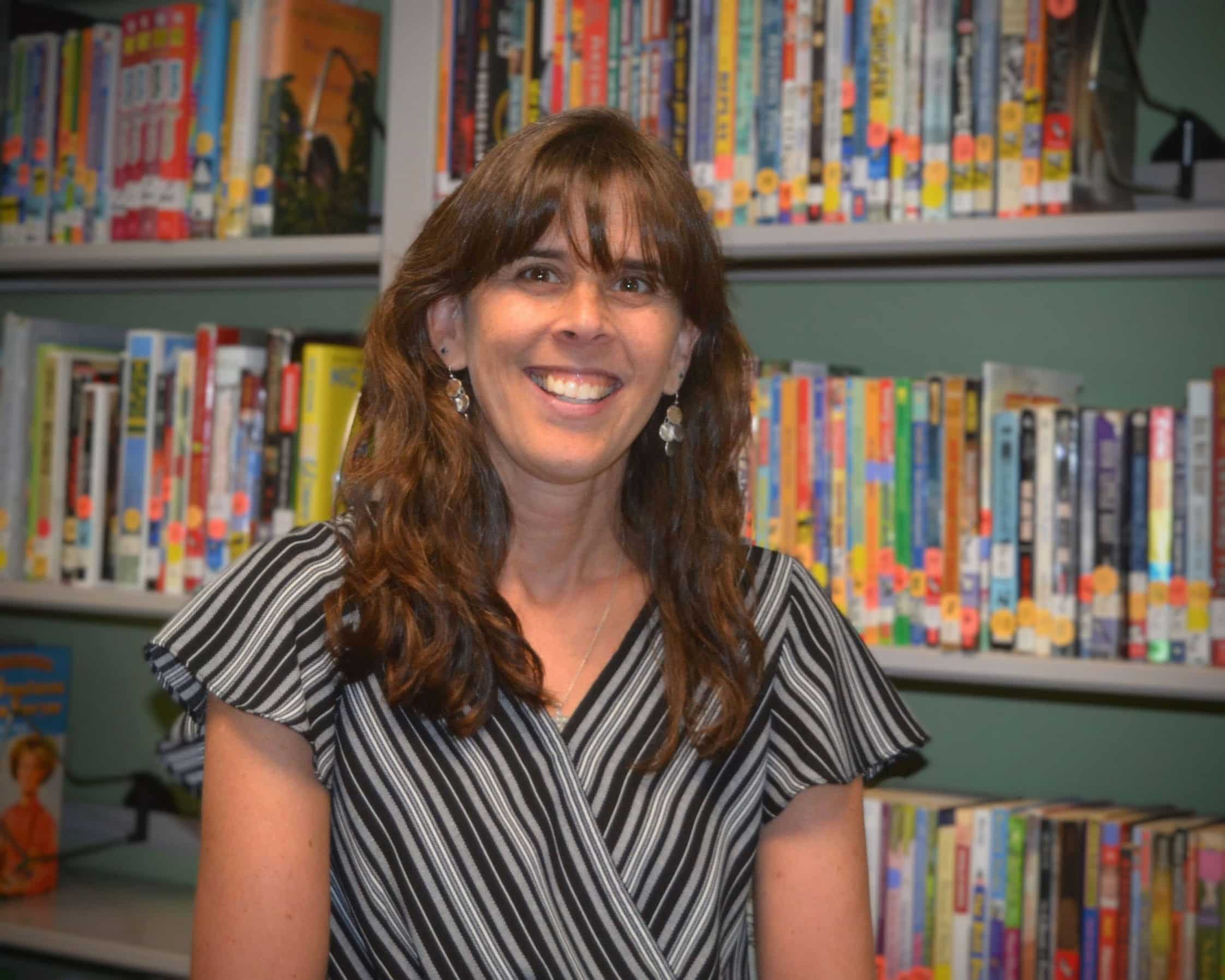 A woman smiling in front of a bookshelf.