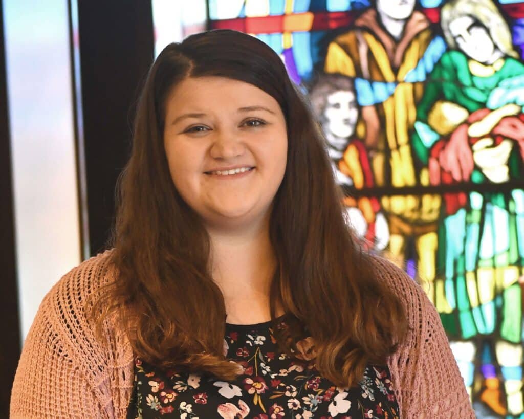 A young woman standing in front of a stained glass window.