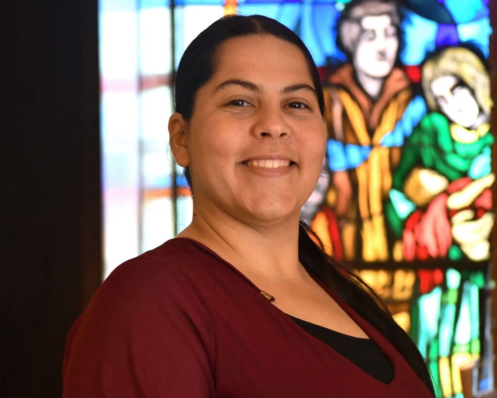A woman smiling in front of a stained glass window.