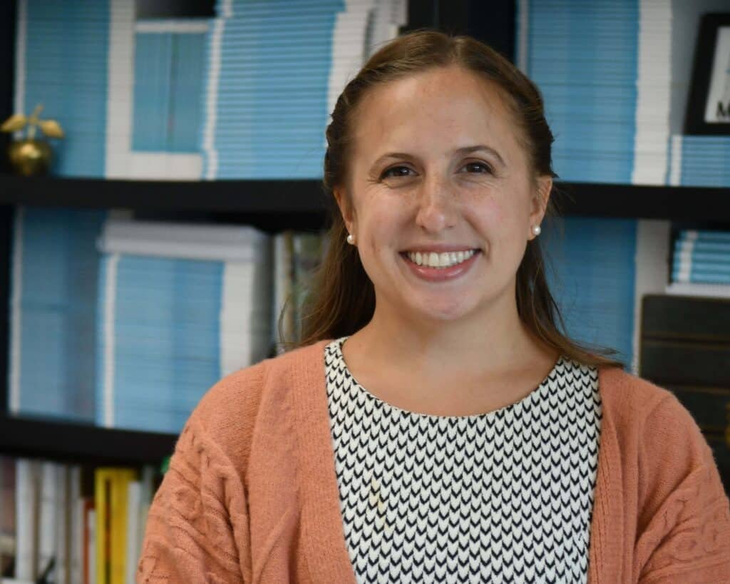 A smiling woman standing in front of a book shelf.