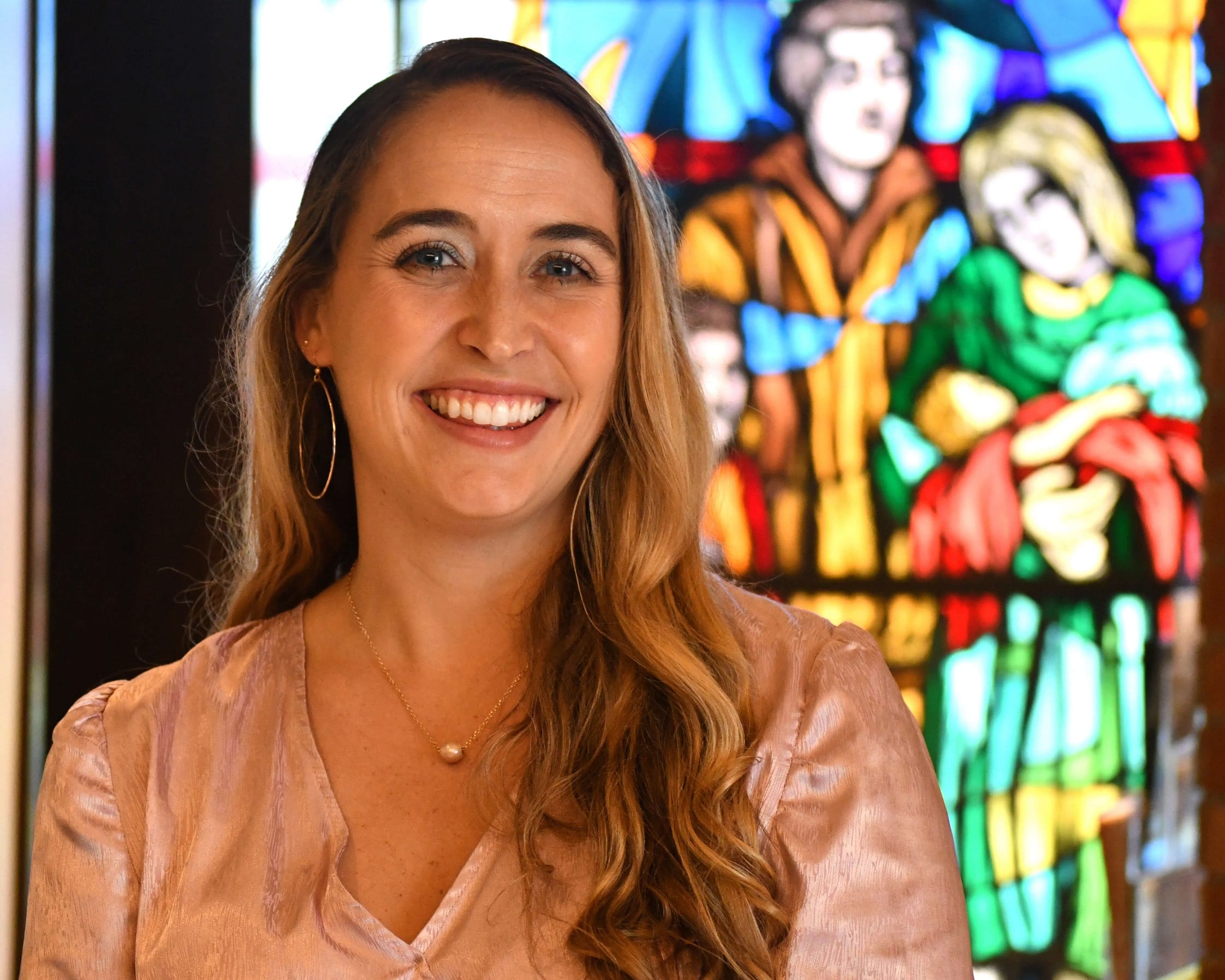 A woman smiling in front of a stained glass window.