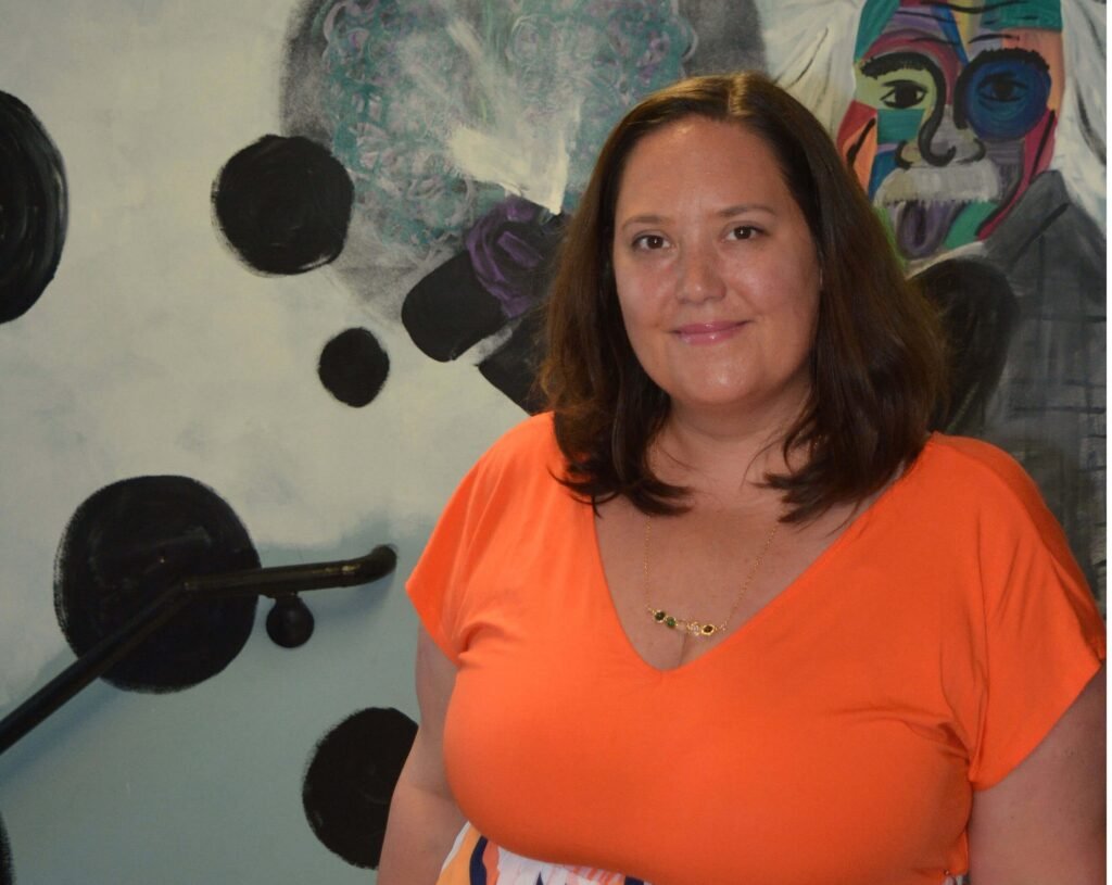 A woman in an orange shirt standing in front of a painting.