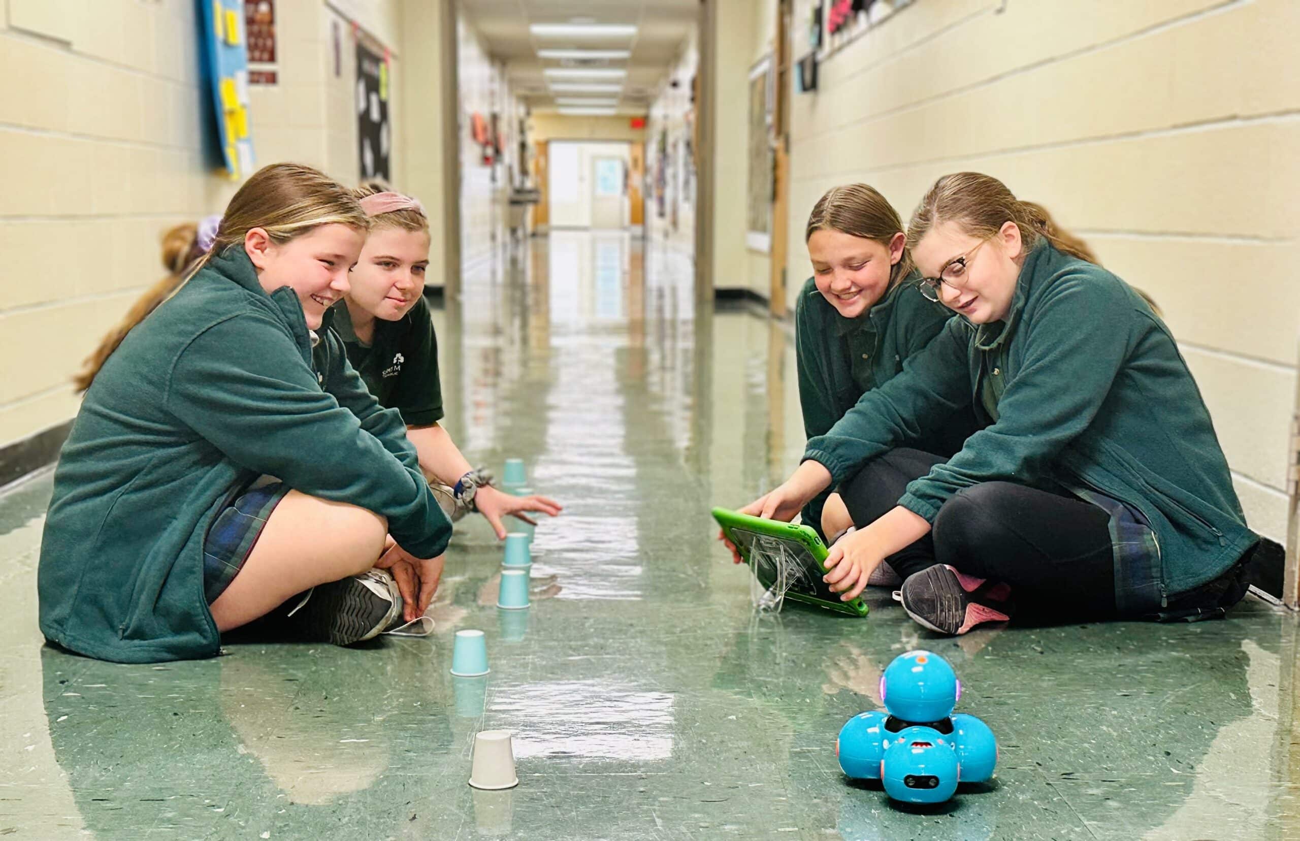 Four girls playing with robots in a hallway.