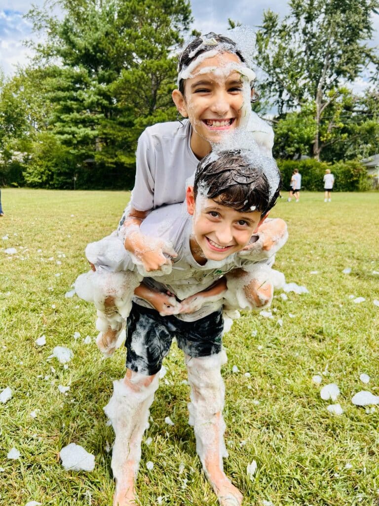Two boys playing in a field covered in foam.