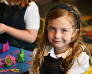 A girl in a school uniform smiles at a table full of toys.