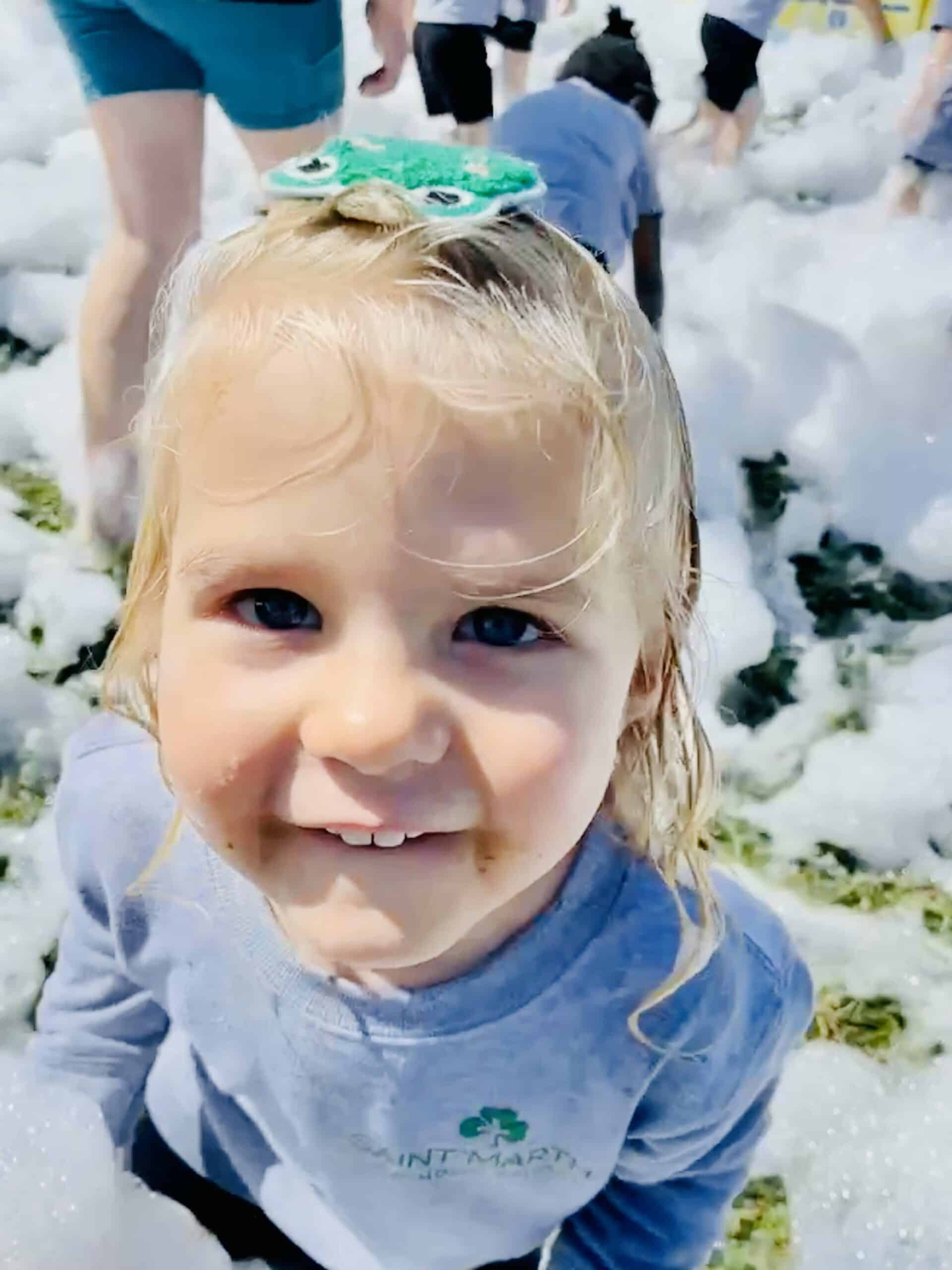 A little girl smiling in a field of foam bubbles.