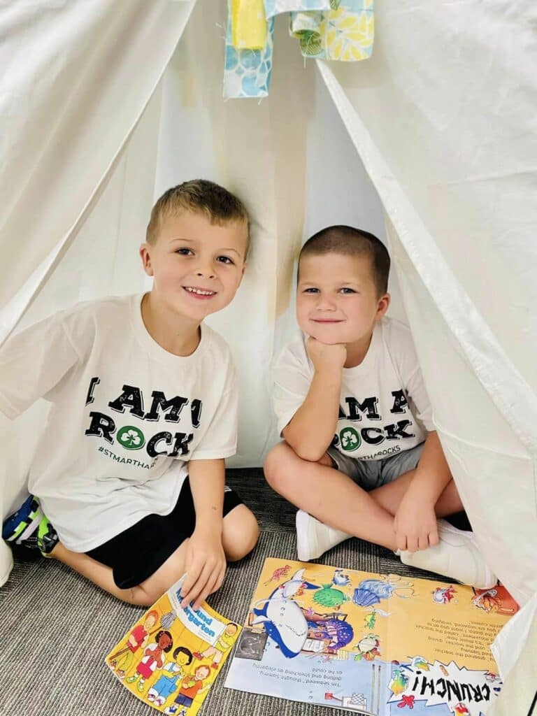 Two boys sitting in a teepee with books.
