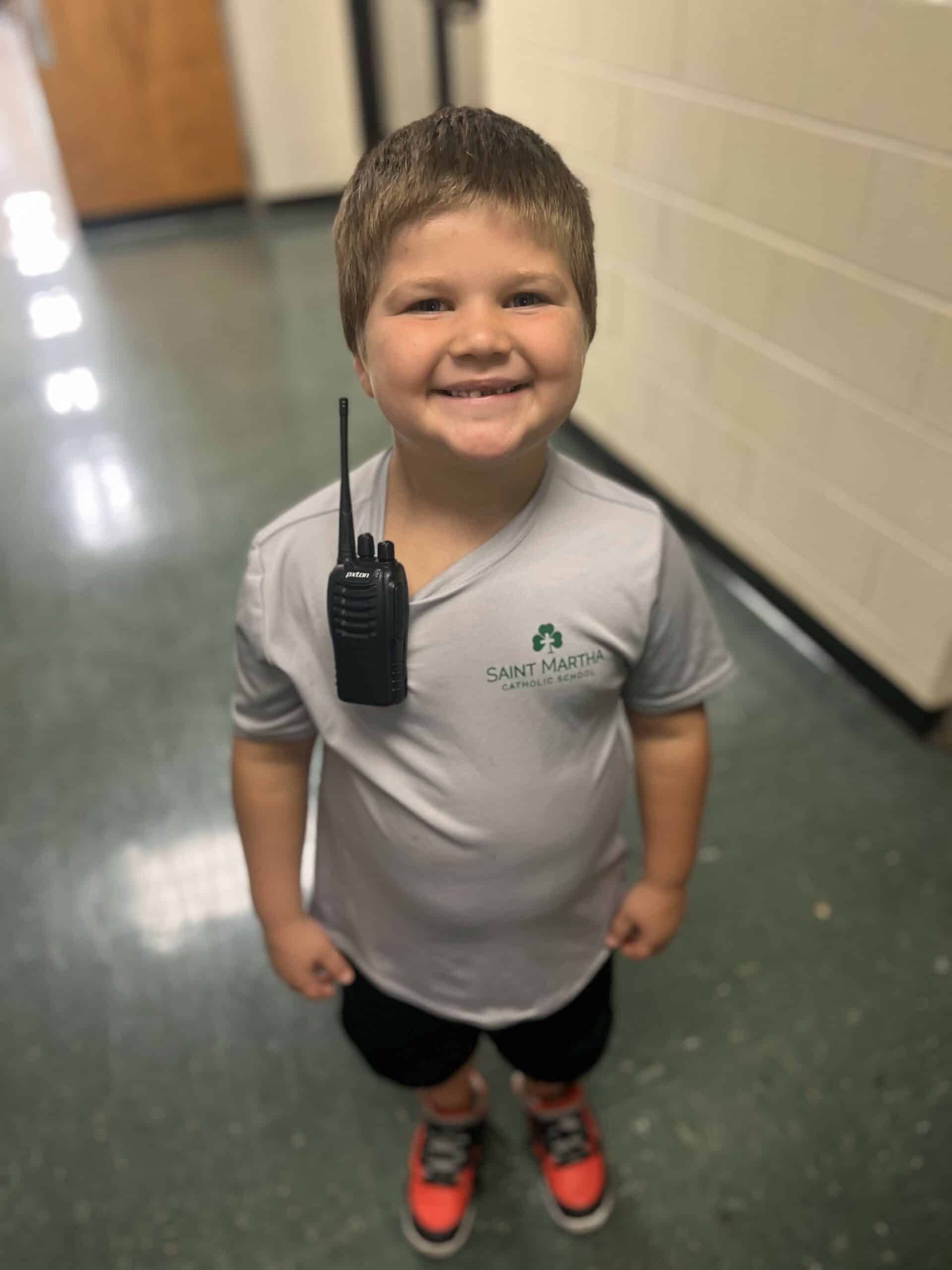 A young boy smiling while holding a walkie talkie.